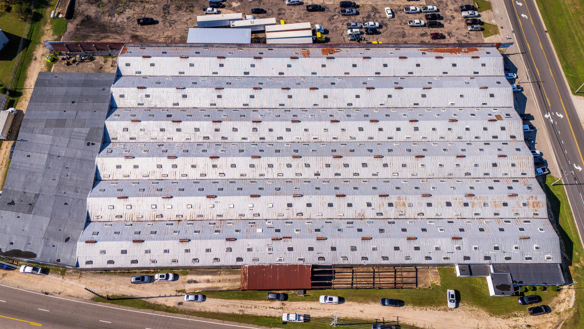 Overhead view of a large industrial metal roof with repeated panel runs, roof transitions, and penetrations