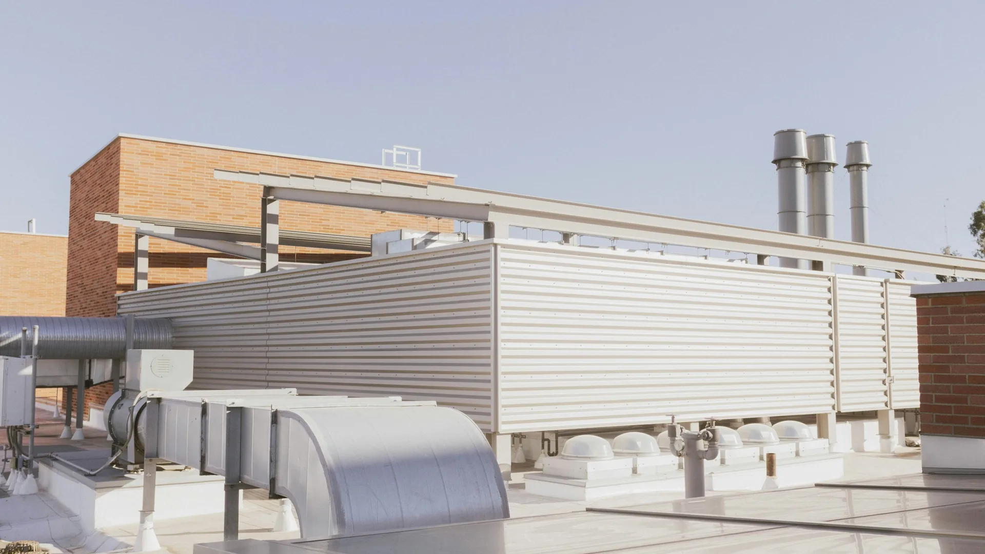 Commercial low-slope roof with HVAC equipment curbs, ductwork, vents, and pipe penetrations