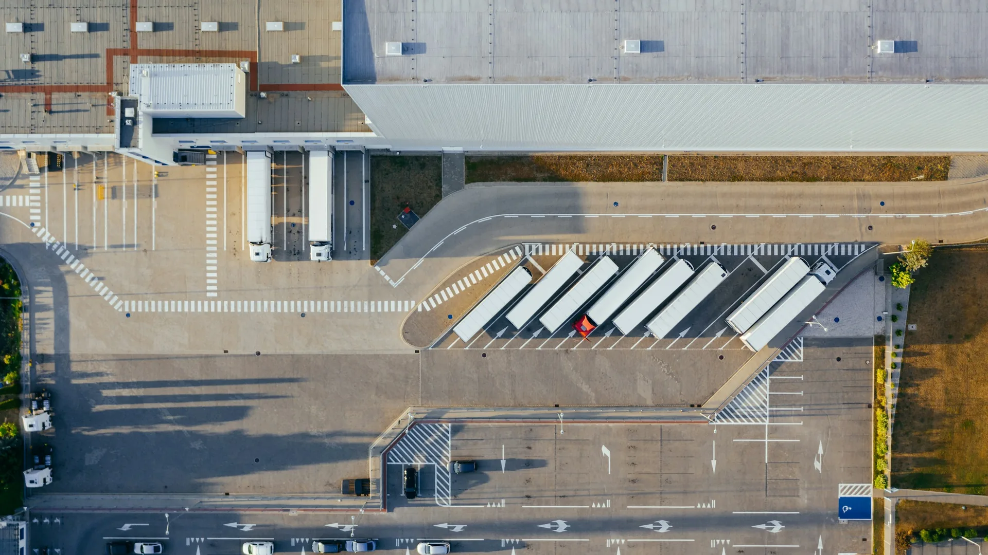 Overhead view of a warehouse roof, loading docks, trailers, and paved service areas