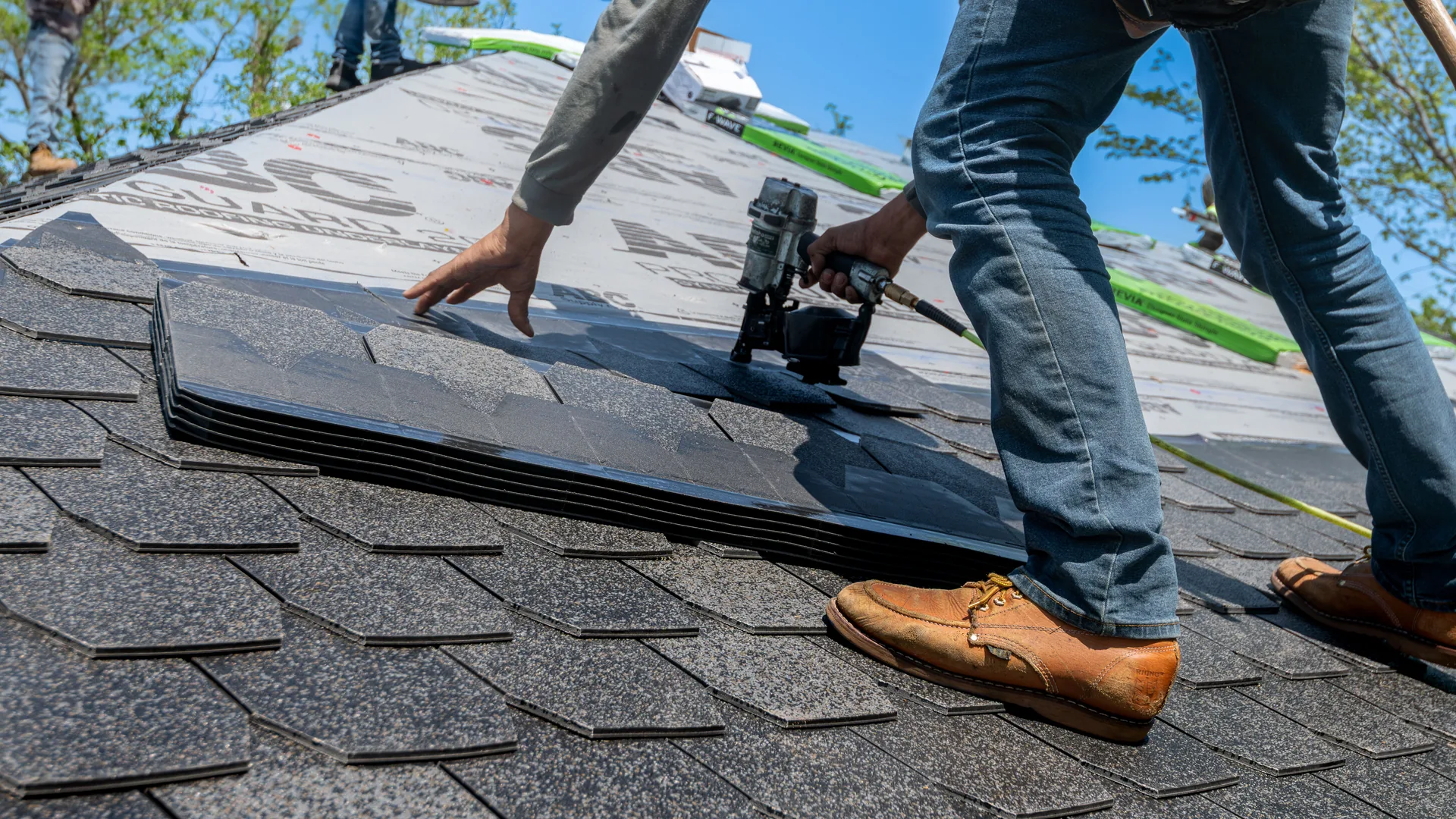 Roofer fastening asphalt shingles over underlayment on a residential roof